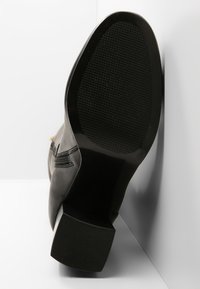 Czarny skórzany botek na wysokim obcasie z teksturowaną podeszwą, zaokrąglonym noskiem i złotymi akcentami metalowymi. Górna część gładka z detalami w postaci przeszyć.