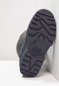 Chaussures grises avec une semelle en caoutchouc noir texturé, présentant un motif de semelle distinct et un accent bleu sur le côté.