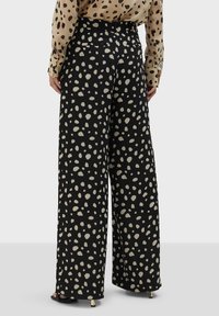 Čierne široké nohavice s bodkovaným vzorom v svetlom béžovej farbe, vyrobené z mäkkej tkaniny s hladkou textúrou a zadnými vreckami.