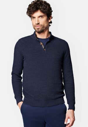 Granatowy sweter dzianinowy o fakturowanym wzorze, z małym kołnierzykiem i dwoma guzikami przy szyi. Ściągacze przy mankietach i na dole.