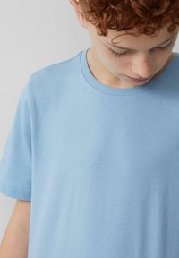 Lichtblauwe katoenen t-shirt met een ronde hals, korte mouwen en een soepele structuur. Bevat subtiele stiksels langs de randen.