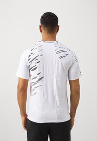 Camiseta atlética blanca con una superficie texturizada, con patrones abstractos negros en la parte posterior. Etiqueta "VENUM PERFORMANCE" en el cuello.