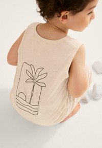 Beige tanktop met een zwarte palmboom en zon lijntekening op de achterkant. Zachte stof, mouwloos ontwerp en een relaxte pasvorm.