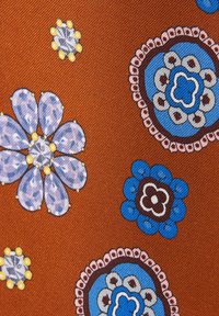 Tissu orange avec des motifs floraux bleus, violets et blancs, présentant des pétales détaillés et des dessins circulaires ressemblant à des mandalas.