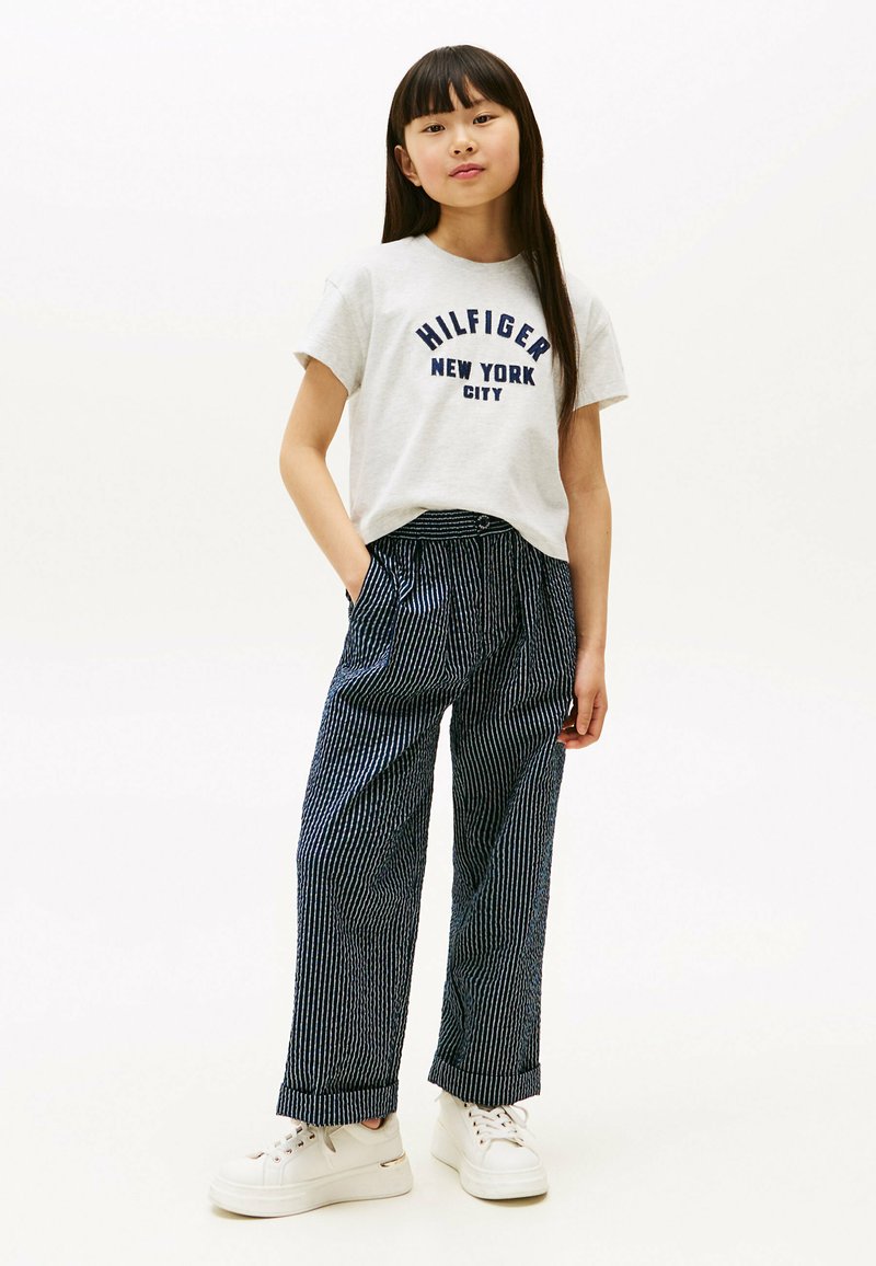 Szara bawełniana koszulka z granatowym napisem "HILFIGER NEW YORK CITY", w połączeniu z granatowymi spodniami o szerokich nogawkach w paski oraz białymi trampkami na sznurówki.