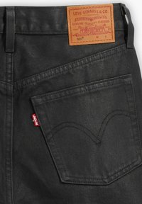 Černé džínové kalhoty s hnědou koženou nášivkou na pase, se dvěma zadními kapsami a červeným štítkem Levi's blízko pravé kapsy.