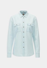 Ljust blå denimskjorta med knappstängning, två bröstfickor och bruna knappar som detaljer. Har långa ärmar och en klassisk krage.