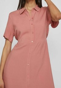 Abito a maniche corte, con bottoni, realizzato in morbido tessuto rosa. Presenta un colletto, una texture liscia e una silhouette dritta con un dettaglio della cucitura centrale.