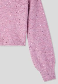 Manica di un morbido maglione rosa a maglia con piccoli paillettes lucidi sparsi, polsino e orlo a coste su uno sfondo grigio chiaro.