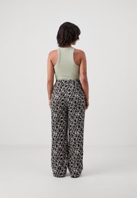 Top a spalla ribbed verde chiaro e pantaloni a gamba larga neri con un motivo astratto bianco, mostrati di spalle su uno sfondo neutro.