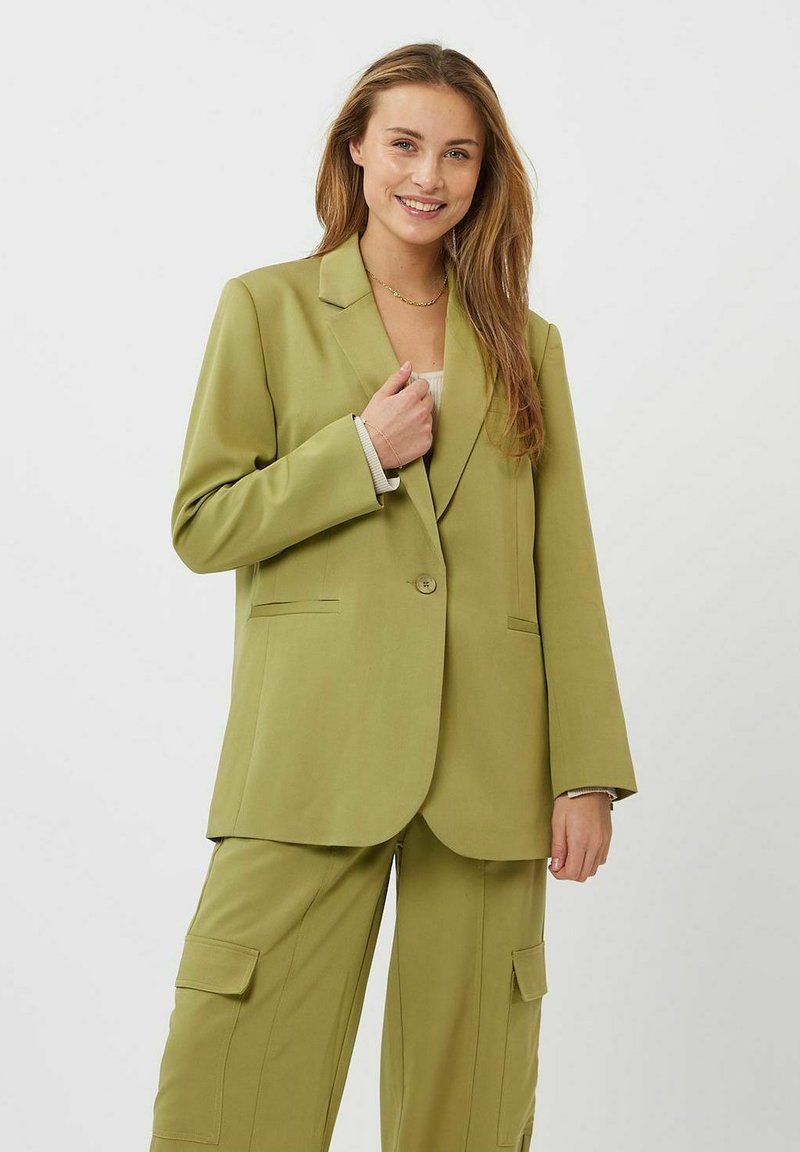 Blazer verde con un solo botón, solapas muesca y bolsillos laterales, combinado con pantalones cargo a juego que presentan bolsillos con solapa. Textura suave.