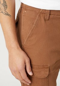 Braune Baumwoll-Cargohosen mit einer Seitentasche und sichtbaren Ziernähten. Verfügt über eine Slim-Fit-Passform und eine strukturierte Oberfläche.
