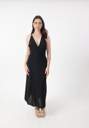 Abito lungo senza maniche di colore nero con scollatura a V profonda, busto aderente, gonna morbida e design minimalista. Abbinato a dei sandali leggeri con cinturini.