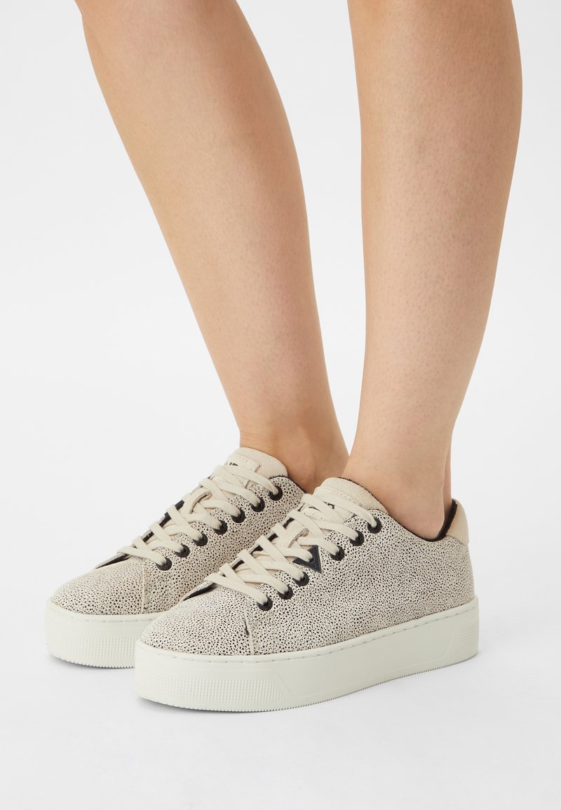 Baskets couleur crème avec une surface texturée, bout rond, œillets noirs et lacets beiges. Semelle blanche surélevée offrant une hauteur supplémentaire.