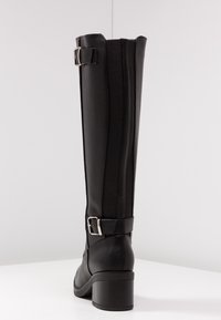 Czarny skórzany kozak do kolan z elastycznymi panelami po bokach, dwoma srebrnymi klamrami i blokowym obcasem na białej powierzchni na tle jasnoszarym.