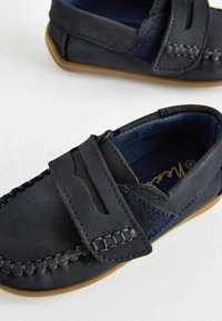 Scarpe in pelle blu navy con un pannello a tessitura testurizzata, caratterizzate da un design mocassino cucito e una suola in gomma beige. Chiusura in velcro per un'agevole calzata.