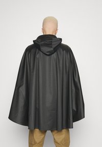 Svart huva i slätt, glänsande tyg. Har en lös, flödande design med en rundad nederkant. Enkel och minimalistisk, utan synliga beslag.