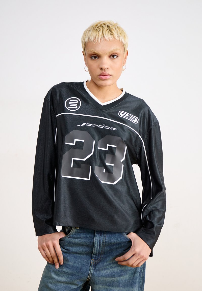 Svart langermet jersey med V-hals, prydet med hvite detaljer og et stort "23" på forsiden. Laget av glatt, lett materiale.