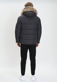 Chaqueta acolchada gris oscuro con capucha forrada de piel, diseño acolchado y puños acanalados, combinada con pantalones negros y zapatillas blancas.