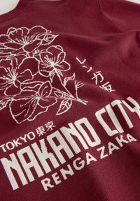 Bordowy sweter z białym kwiatowym wzorem i napisem "TOKYO NAKANO CITY RENGAZAKA", z okrągłym dekoltem i miękką fakturą.