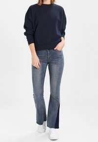 Sweat-shirt marine à épaules tombantes, associé à un jean évasé bleu clair avec des fentes latérales, complété par des baskets blanches.