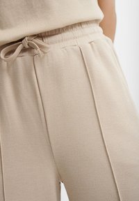 Jasno-beżowe dresy wykonane z miękkiego materiału, z elastycznym pasem w talii i sznurkiem do regulacji oraz subtelnymi poziomymi detalami w ściegach.