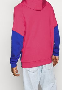 Hoodie i rosa och blått. Har en avslappnad passform med kontrasterande ärmar, mjuk textur och ribbstickade cuffs.