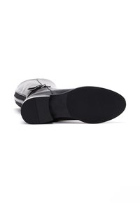 Botín de cuero negro con punta redondeada, cremallera lateral y suela de goma negra texturizada. Presenta un acento plateado a lo largo del lateral.