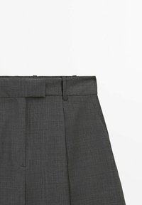 Pantalons gris ajustés avec une taille plate, passants de ceinture et plis marqués. Le tissu présente un motif texturé subtil.