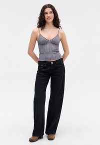 Striped gray fitted top with thin straps paired with black wide-leg pants featuring a front button closure and side pockets. Brown heeled shoes.