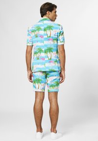 Chemise à manches courtes et shorts en bleu clair, ornés de flamants roses et d'arbres tropicaux verts dans un motif tropical. Fabriqué en tissu léger.