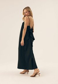 Czarna sukienka bez rękawów o luźnym kroju, z niskim dekoltem z tyłu i falbaną z boku. Nosi się ją z cielistymi sandałkami na obcasie typu kitten heel.