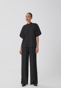 Svart skjorta med korta, volymösa ärmar; matchad med vida svarta mönstrade byxor med diamanttextur.