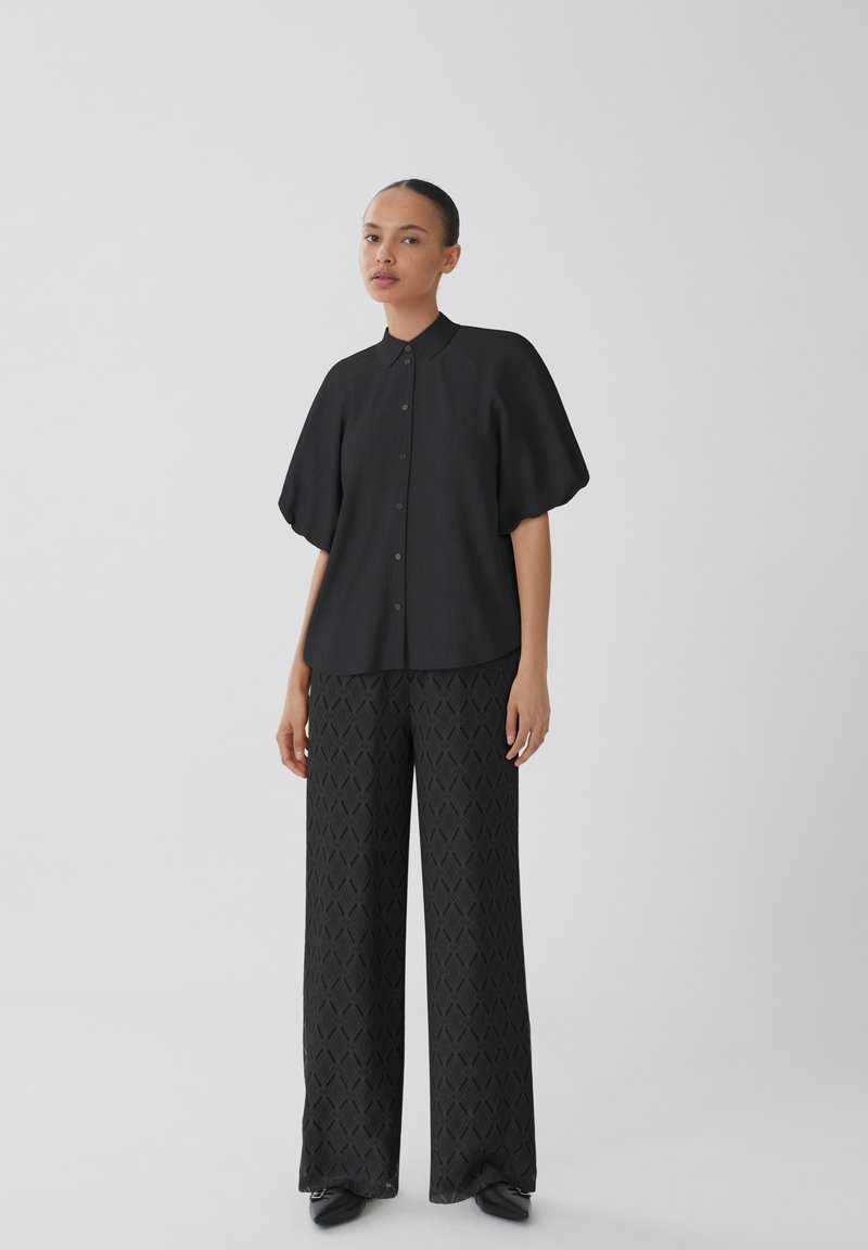 Svart skjorta med korta, volymösa ärmar; matchad med vida svarta mönstrade byxor med diamanttextur.
