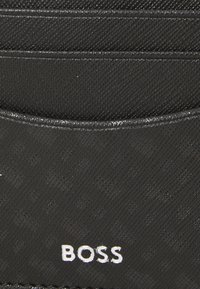 Portafoglio nero realizzato in materiale testurizzato con una finitura liscia, dotato di più scomparti per carte e del nome del marchio "BOSS" in argento.