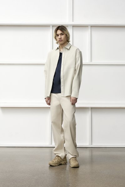 Chemise boutonnée beige clair sur un top bleu marine, associée à un pantalon beige assorti et des baskets beiges, sur fond blanc.