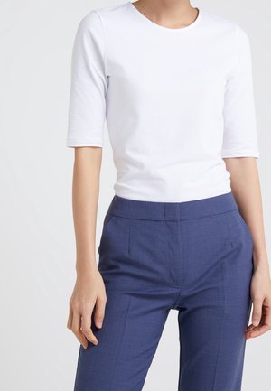 Biała, krótka koszulka z krótkim rękawem i okrągłym dekoltem, zestawiona z granatowymi, dopasowanymi spodniami o gładkiej fakturze i płaskim przodzie.