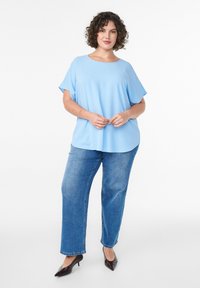 Jasnoniebieska bluzka z krótkimi rękawami i zaokrąglonym dekoltem, zestawiona z niebieskimi dżinsami i ciemnobrązowymi butami z zaokrąglonym noskiem.