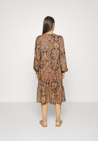 Vestido de mangas largas en marrón con diseño de paisley negro, ajuste holgado, hasta la rodilla y con dobladillo en capas. Hecho de una tela ligera.
