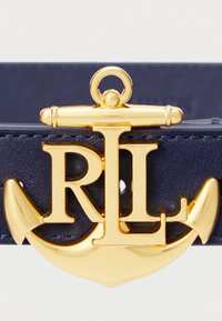 Cinto de couro azul-marinho com fivela dourada em forma de âncora, apresentando letras entrelaçadas "RL", textura suave e detalhes metálicos.