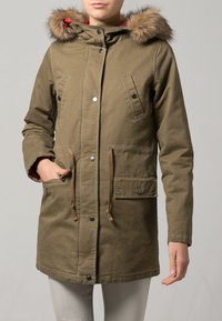 Olivgrön parka-jacka med foder i päls, tryckknappar och justerbara dragsnören. Har två framfickor och foder på insidan.