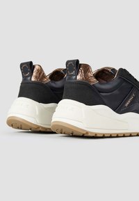 Schwarze Leder- und Wildledersneaker mit bronzefarbenem Metallic-Akzent und weißer, klobiger Sohle. Verfügt über Zugschlaufen und strukturierten Fersenbereich.