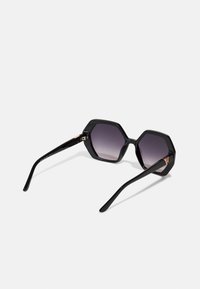 Ochelari de soare octagonali negri cu lentile gradient purpurii. Rame din plastic lucios cu brațe subțiri și curbe negre, și un accent auriu pe balama.