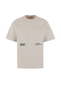 Světlobéžové tričko s krátkým rukávem vyrobené z bavlny. Na přední straně se nachází logo "SAC" a text "SATURDAY ATHLETICS CLUB" v zelené barvě.