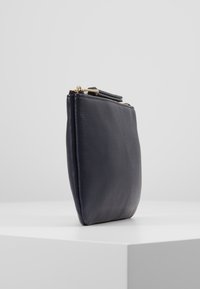 Pochette en cuir bleu marine avec une texture lisse, de forme rectangulaire et une fermeture éclair dorée sur le dessus. Design minimaliste sans motifs visibles.