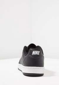 Zapatilla negra de cuero con suela blanca y logo. Presenta un upper texturizado, un collar acolchado y detalles perforados para mayor transpirabilidad.