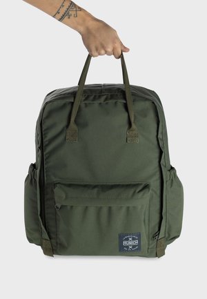 Mochila de tela verde con dos asas superiores, bolsillo exterior, bolsillos laterales de malla y una etiqueta con el logo en la parte frontal. Textura lisa, forma rectangular.