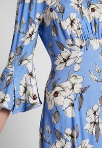 Blue floral dress featuring white flowers with dark accents, a flared sleeve design, and a soft, smooth fabric texture.
