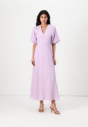 Light purple, ribbed maxi dress with a V-neck and wide flutter sleeves, featuring a fitted waist and flowing skirt. Model wearing gold strappy heels.