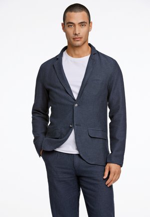 Blazer de mezcla de lino azul oscuro con solapas de muesca, dos botones y bolsillos delanteros, superpuesto a una camiseta blanca de tela texturizada.